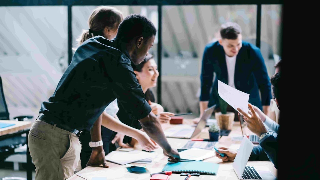 A diverse group of colleagues collaborates around a table, reviewing documents and sharing ideas in an office.