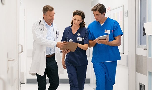 A group of healthcare professionals walking and discussing patient care in a bright hospital corridor.