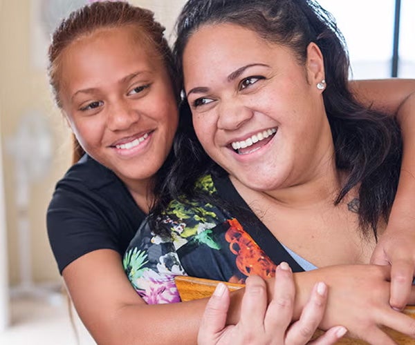 A joyful woman and teenage girl sharing a warm embrace and bright smiles.